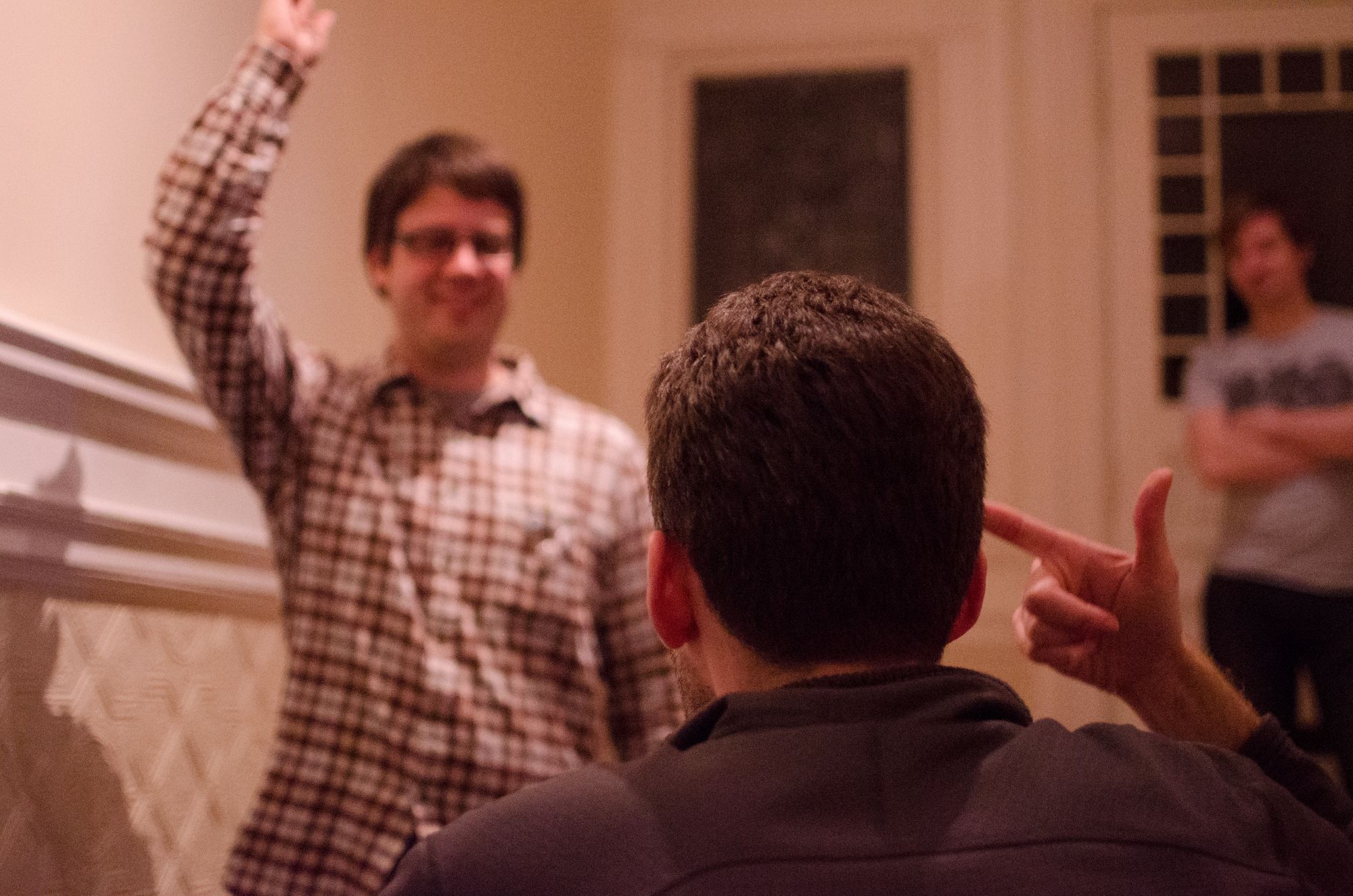 Two men are looking at each other. In the foreground, a man points to his head. In the distance, his opponent is pointing towards the air. The two are playing the folk game Standoff.